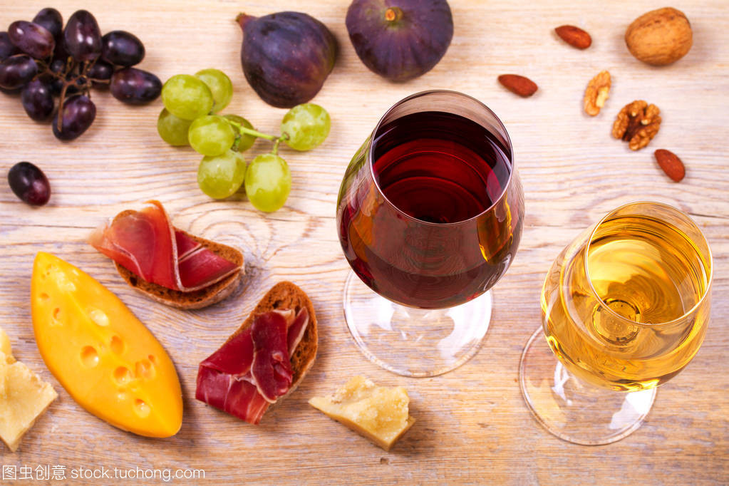 紅色和白色奶酪、 火腿、 無花果和葡萄與葡萄酒杯。木制的桌子上的酒杯。葡萄酒的靜物